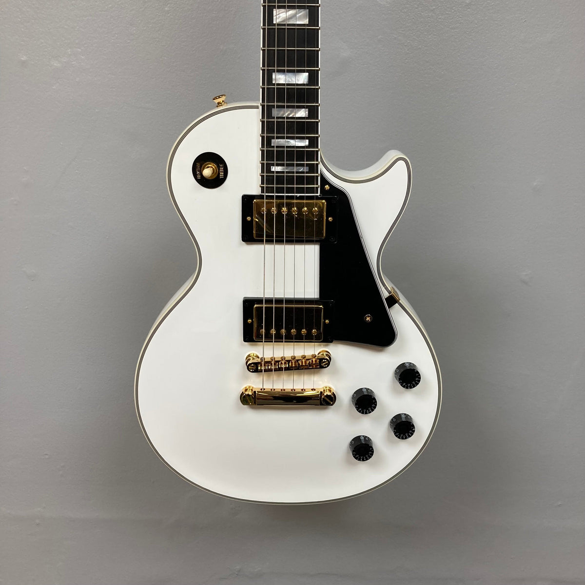 Epiphone Les Paul Custom Inspired by Gibson Alpine White electric guitar with gold hardware, black accents, and hardshell case.