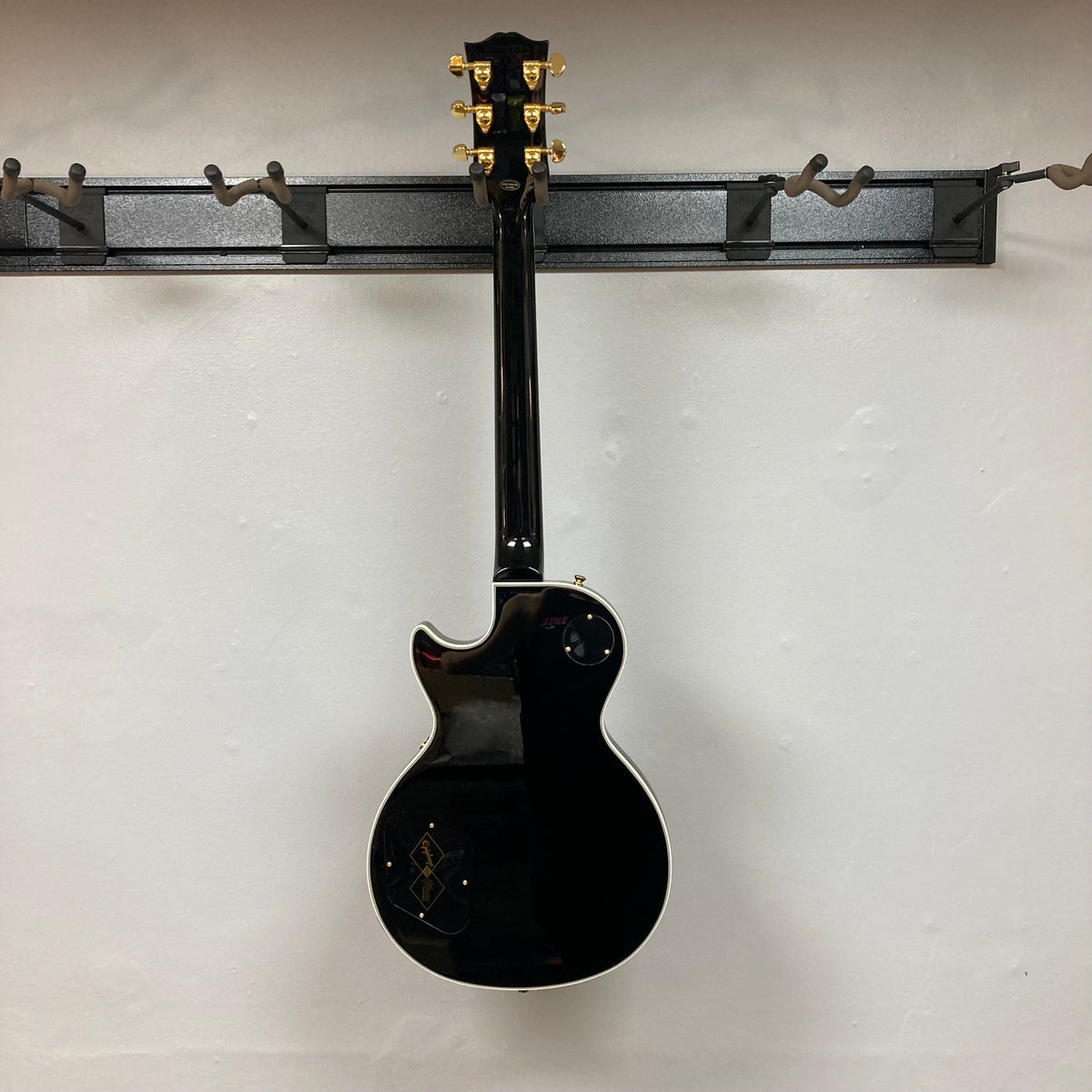 Epiphone Les Paul Custom Inspired by Gibson Ebony w/Case, featuring a mahogany body, maple top, and Gibson USA humbuckers, displayed on a wall.
