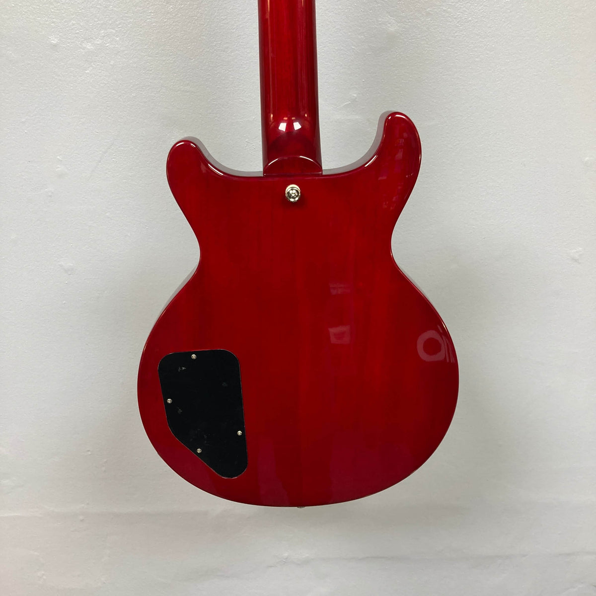 The back of the Epiphone Les Paul Special Double Cut Cherry Red w/Gigbag by Epiphone, showing its glossy finish, black cover plate, and neck joint detail, is pictured against a plain white wall.