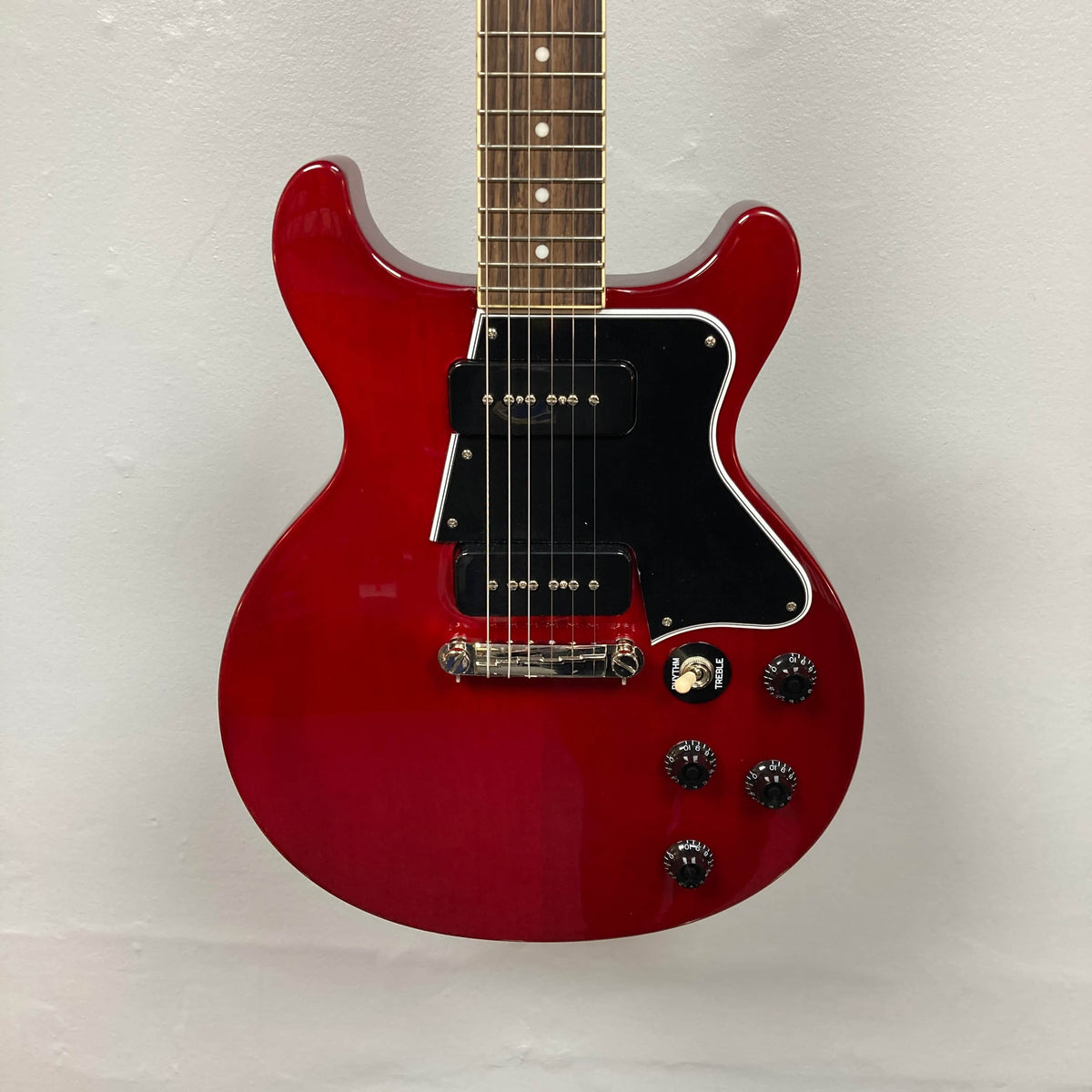 An Epiphone Les Paul Special Double Cut Cherry Red electric guitar with gigbag, featuring dual pickups, four control knobs, black pickguard, by Epiphone. Set against a plain light background.
