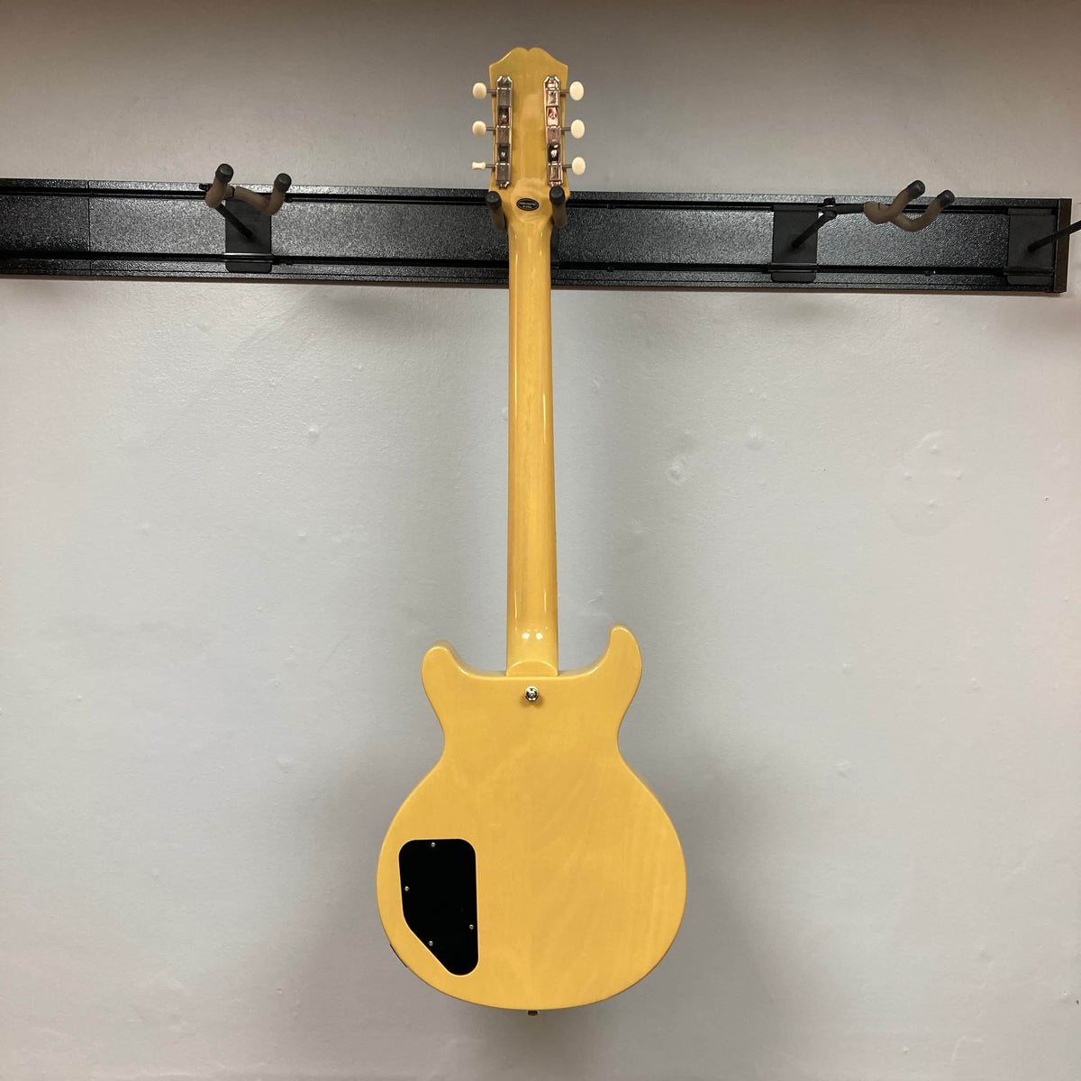 An Epiphone Les Paul Special Double Cut TV Yellow electric guitar with gigbag hangs on a wall rack, displayed from the back with its electronics cover plate visible.