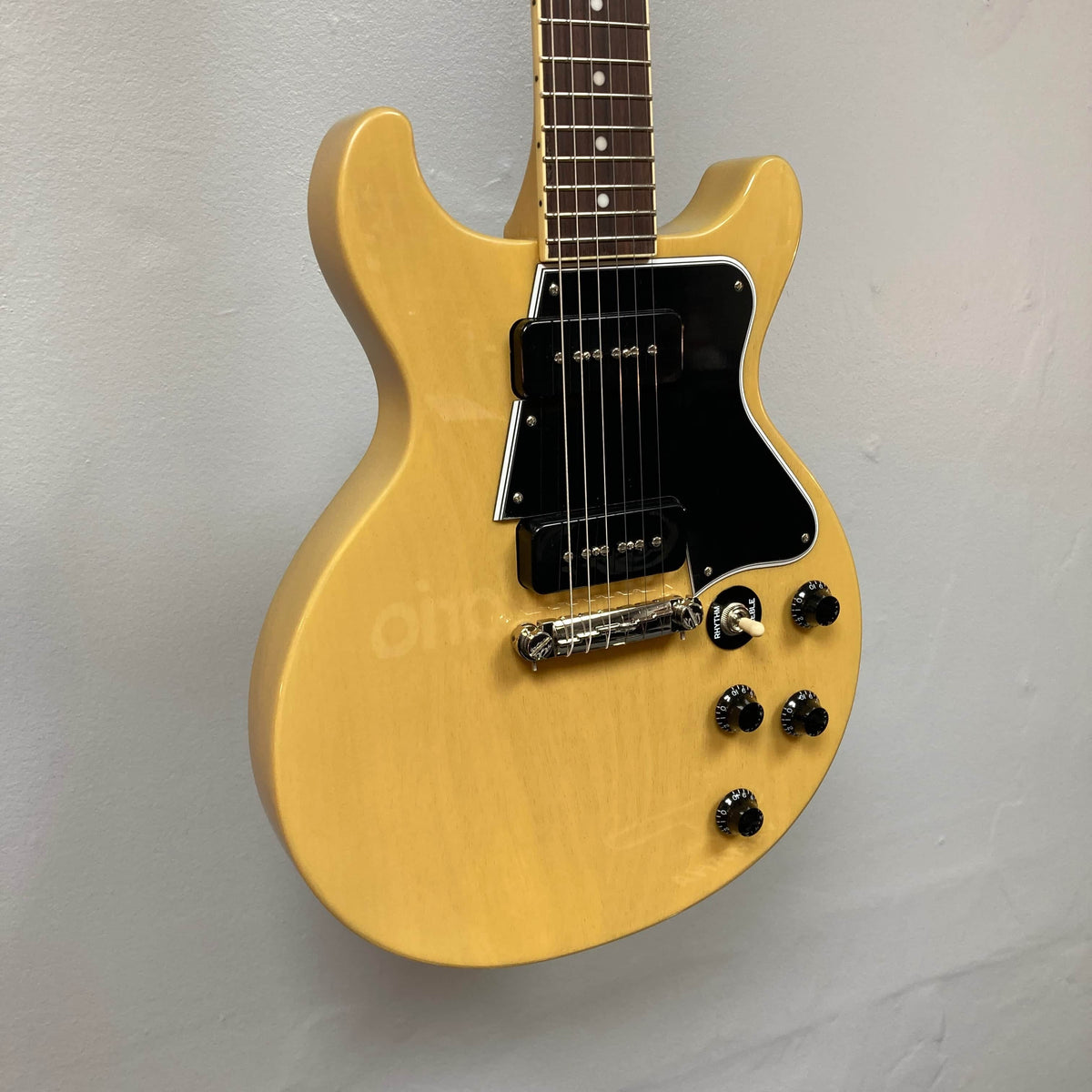 An Epiphone Les Paul Special Double Cut TV Yellow electric guitar with a 60s SlimTaper neck, black pickguard, four control knobs, and dual pickups is shown against a plain light-colored wall. Includes gigbag. Brand: Epiphone.