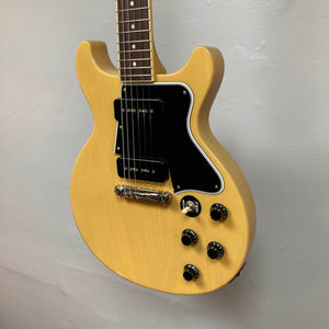 An Epiphone Les Paul Special Double Cut in TV Yellow with a gigbag hangs against a plain light-colored wall.