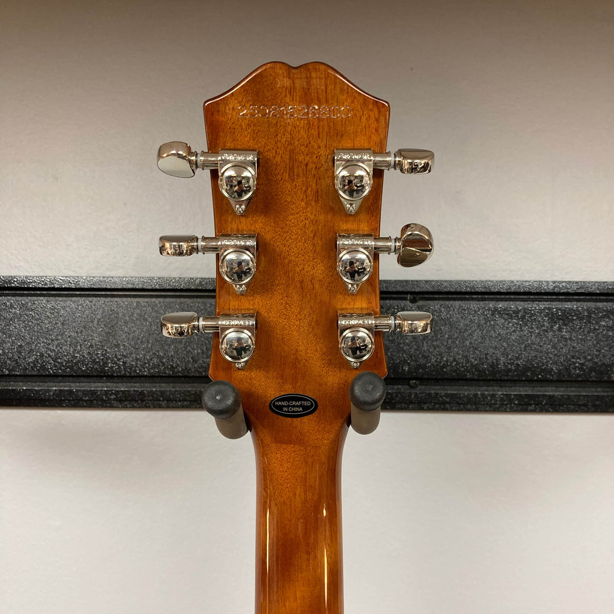 The back of an Epiphone Les Paul Standard 60s Ebony w/Gigbag guitar headstock with six metal tuning pegs is shown on a wall hanger against a white background.
