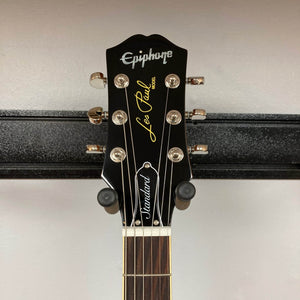 Headstock of the Epiphone Les Paul Standard 60s Ebony w/Gigbag by Epiphone, with tuning pegs, logo, and fretboard visible—a classic nod to vintage Gibson Les Paul design, set against a plain wall.