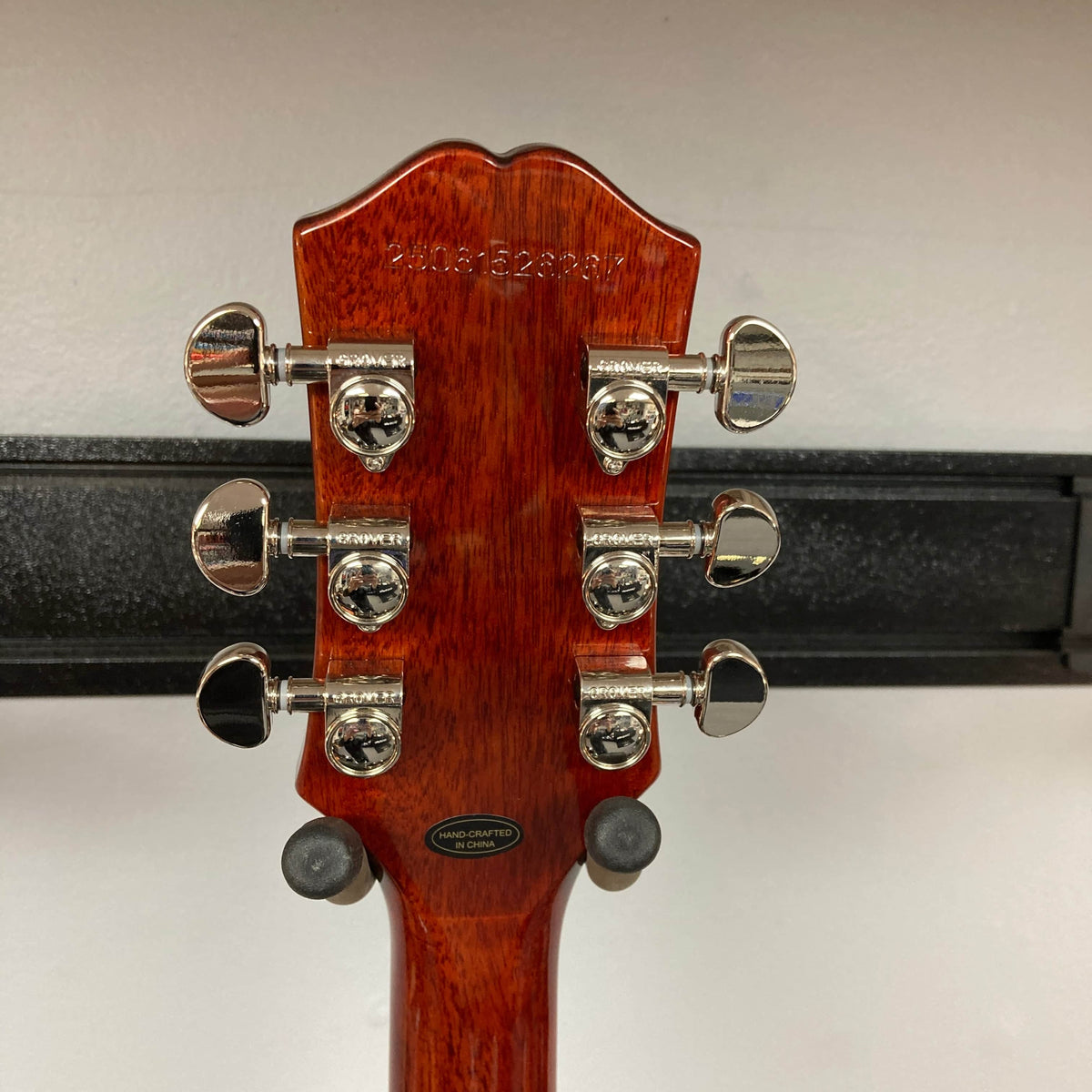 Close-up of the back of an Epiphone Les Paul Standard 60s Figured Iced Tea Burst w/Gigbag headstock, showing six tuning pegs, a serial number, and a "hand crafted in China" label.