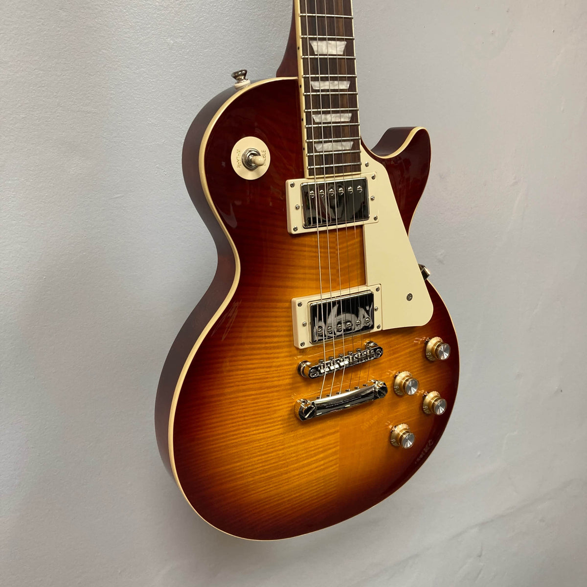 Epiphone Les Paul Standard 60s Figured Iced Tea Burst electric guitar with white pickguard, dual humbuckers, four control knobs, and included gigbag, displayed against a plain light-colored wall.