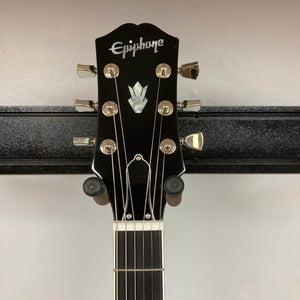 The Epiphone SG Modern Figured Iguana Burst w/GigBag features six tuning pegs on its headstock and a SlimTaper neck, shown hanging on a black wall-mounted guitar holder.