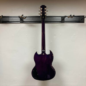 An Epiphone SG Modern Figured Purple Burst w/GigBag electric guitar hangs on a wall rack, shown from the back against an off-white wall. It features a double-cutaway body and silver tuning pegs.