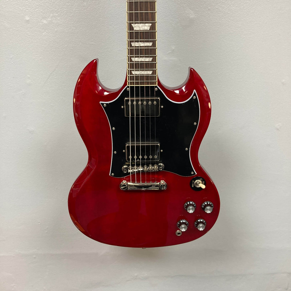 The Epiphone SG Standard Cherry w/Gigbag features a mahogany body, black pickguard, chrome hardware, four control knobs, and dual humbucker pickups, shown here against a plain white wall.