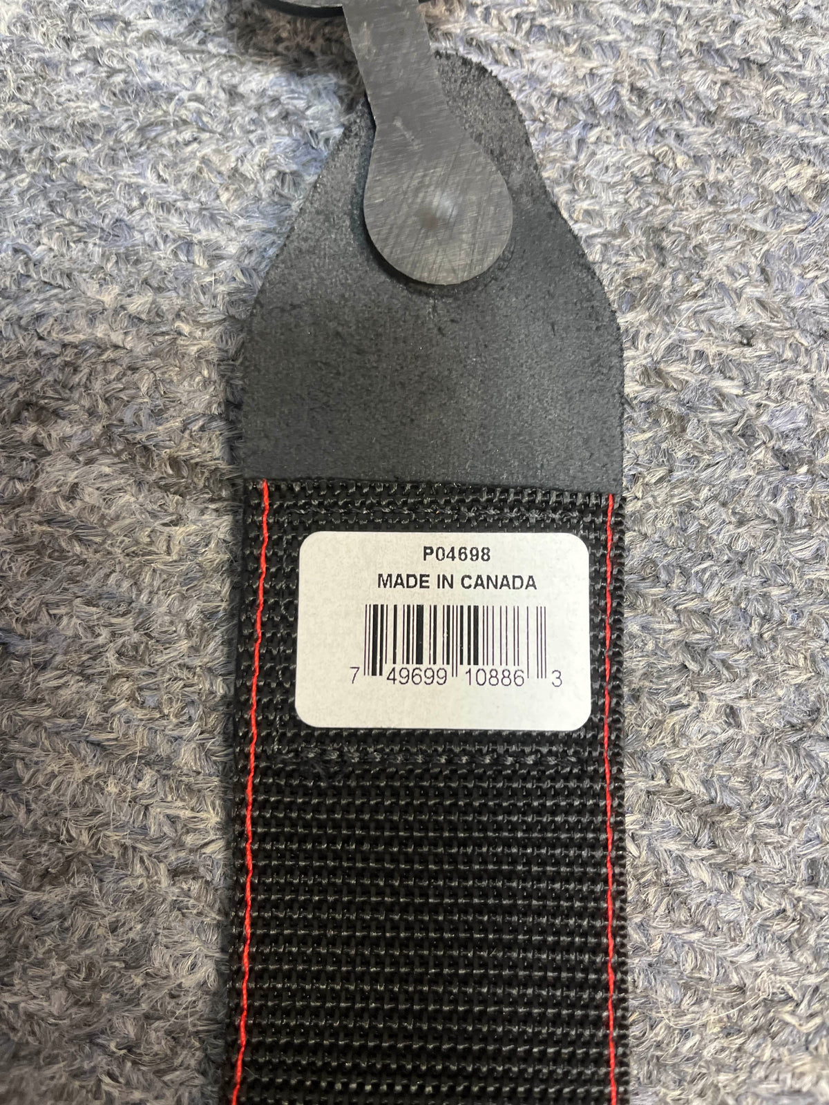A close-up of the Ernie Ball Guitar Strap - Peace & Dove shows its black material with red stitching and a white label marked "P04698 MADE IN CANADA," resting on a textured gray surface.