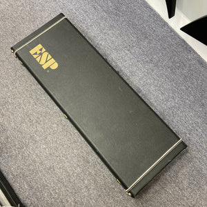 A black rectangular hard case with gold "ESP" lettering, designed for the ESP Standard Eclipse Transparent Cherry Red guitar by Esp, is shown resting on a gray carpeted floor.