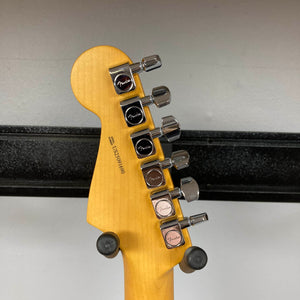 The back of a Fender American Professional II Stratocaster HSS in Dark Night headstock with six tuning pegs and "Fender" logos, displayed on a wall mount.