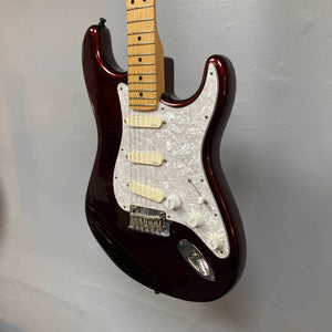 A Fender American Standard Strat upgraded Gilmour EMG DC-20 electric guitar in Bordeaux Metallic with a white pickguard, control knobs, a maple neck, and included case is mounted on a light gray wall.