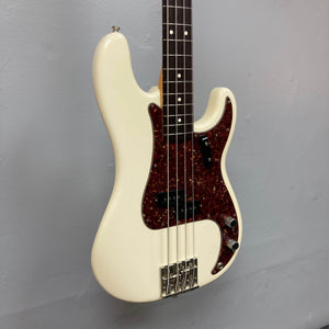A Fender American Vintage '62 Precision Bass Olympic White 2005 w/Case, featuring a dark tortoiseshell pickguard and four strings, is mounted on a light gray wall.
