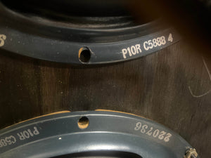 Close-up of two metal rings with serial numbers like "P10R C5888 4" and "220736" on dark wood—likely parts from a 1957 Fender Bassman 5F6 Narrow Panel 40-Watt 4x10" Guitar Combo w/Flight Case by Fender.