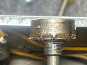 Close-up of a metal component with “MIO A0810 304223” markings and threaded shaft, brown segments, and yellow wires—likely from a Fender 1957 Bassman 5F6 Narrow Panel 40-Watt 4x10" Combo Amp w/Flight Case—in the background.