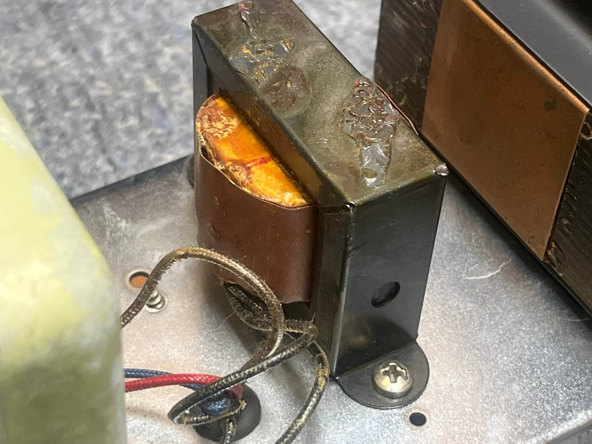 Close-up of a damaged electronic component with melted insulation and exposed wiring from a 1957 Fender Bassman 5F6 Narrow Panel 40-Watt 4x10" Guitar Combo w/Flight Case by Fender, resting on a metal surface.