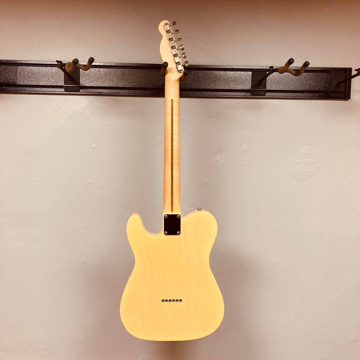 A Fender Custom Shop '51 Reissue Nocaster NOS 2006 electric guitar by Fender, in a light finish, hangs by its neck on a wall-mounted hook, displaying the back of the body and neck against a plain wall.