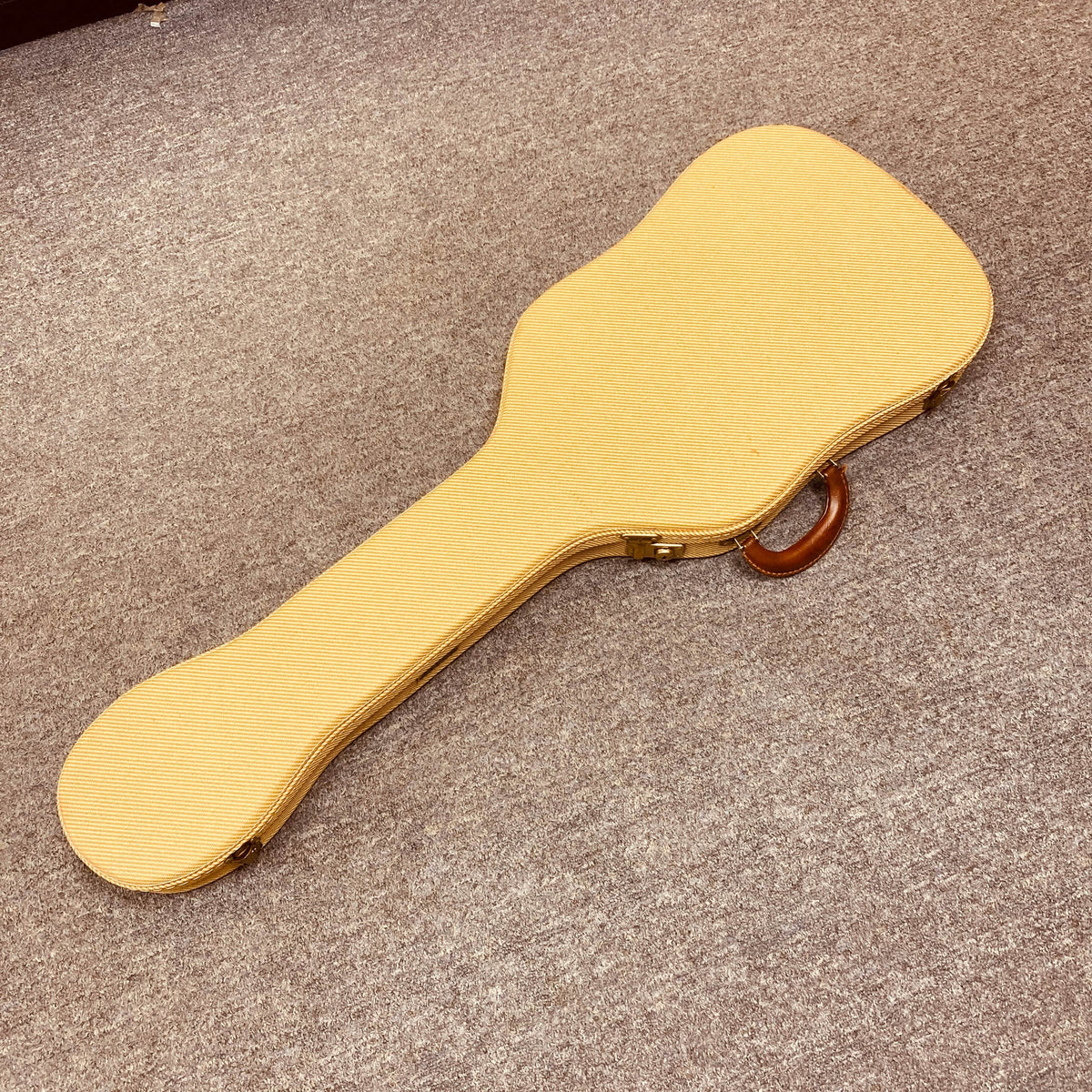 A tan Fender Custom Shop '51 Reissue Nocaster NOS 2006 guitar case with a brown handle rests closed on a beige carpeted floor.