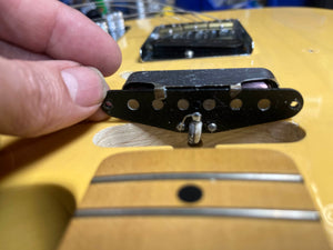 A hand holds a Fender Custom Shop '51 Reissue Nocaster NOS 2006 pickup above a yellow vintage blackguard guitar body, showing the wiring and cavity beneath.