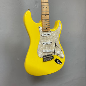 Fender Deluxe Powerhouse Stratocaster MIM Rare Graffitti Yellow displayed on a wall, featuring white knobs and strings, and includes a case.