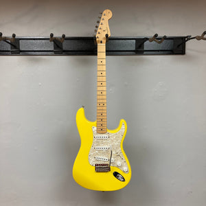 Fender Deluxe Powerhouse Stratocaster MIM in Graffiti Yellow, featuring white knobs and buttons, displayed on a wall.