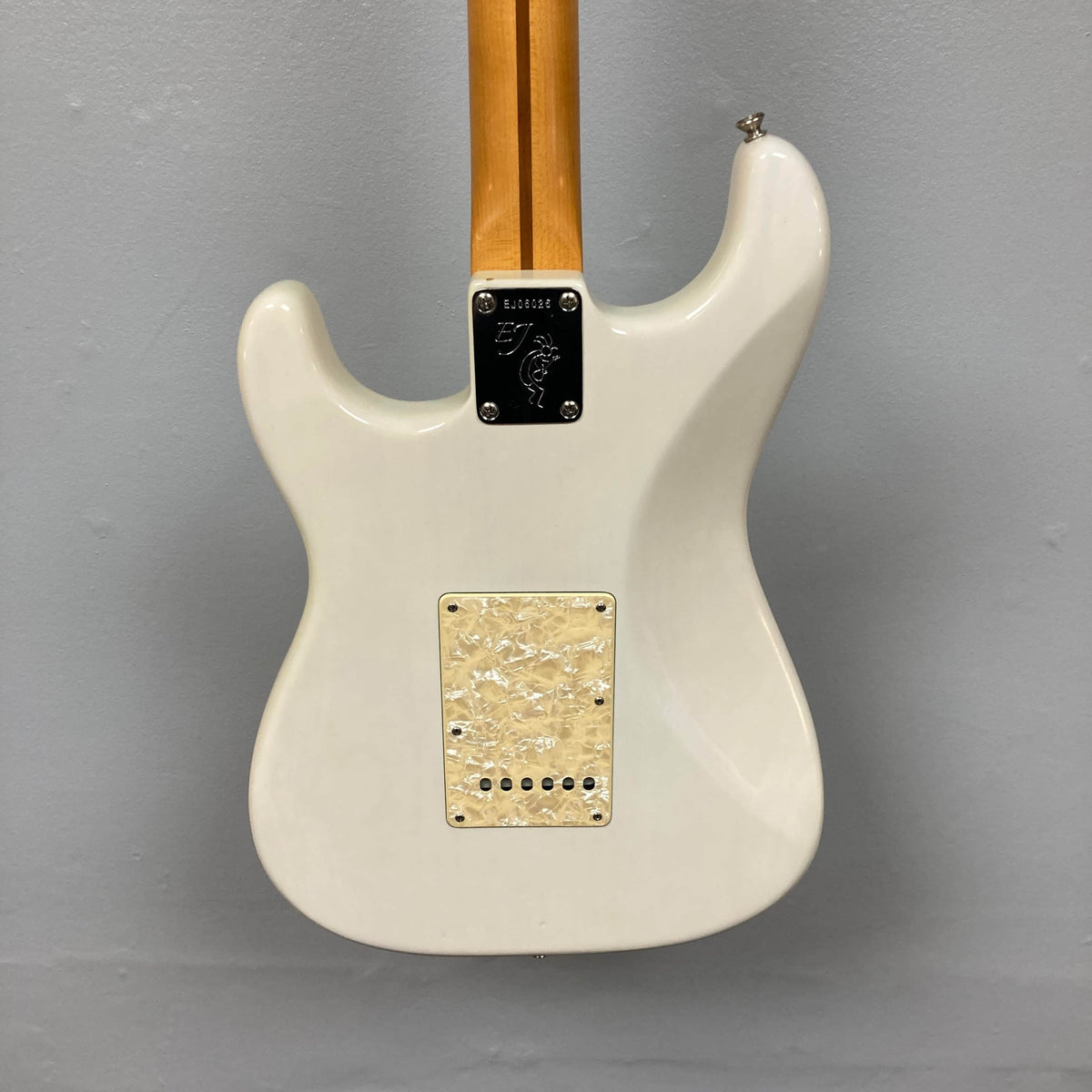 The back of a 2006 Fender Eric Johnson Stratocaster by Fender, featuring a light Maple Fingerboard neck, metal neck plate, and cream-colored back plate, set against a gray wall.