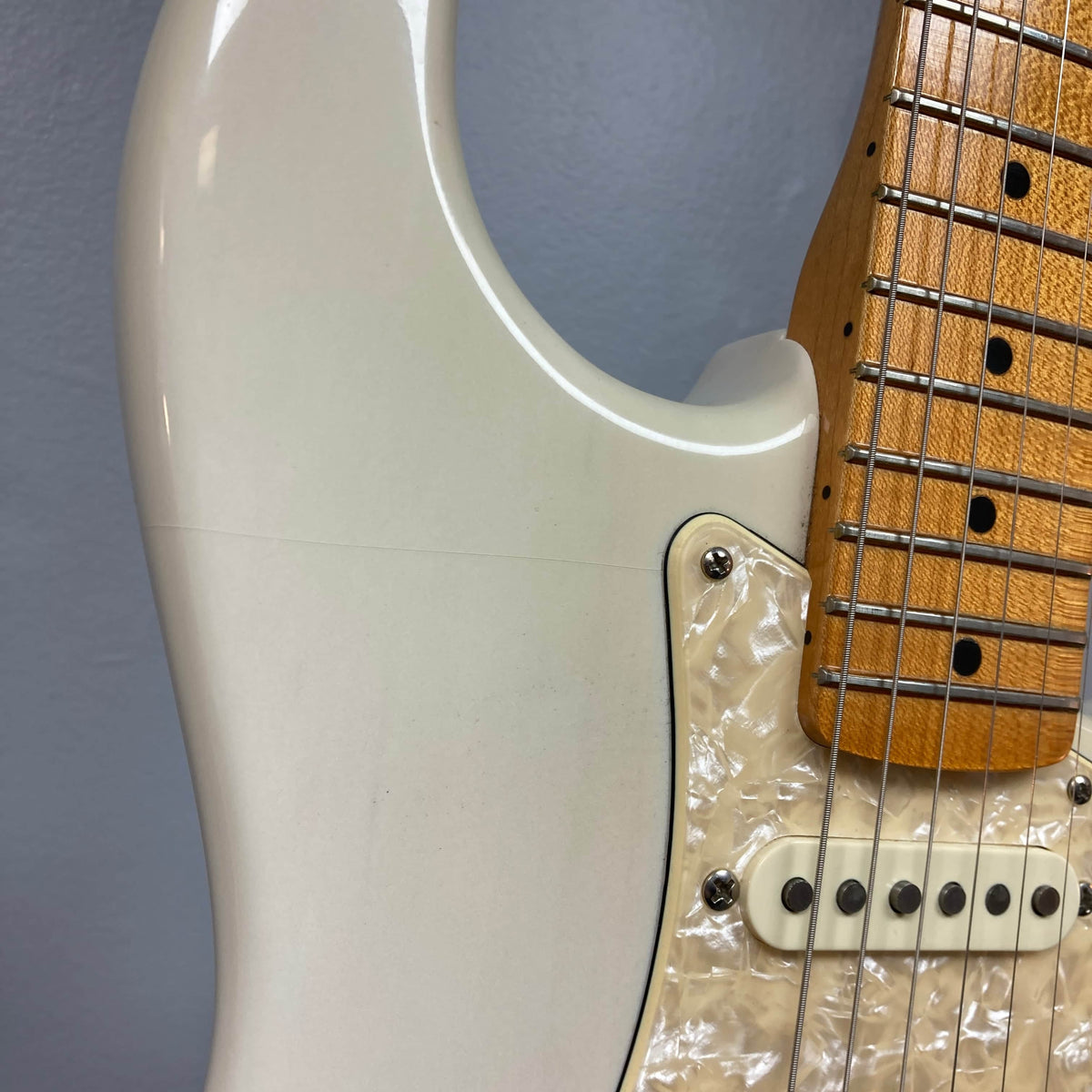 Close-up of a 2006 Fender Eric Johnson Stratocaster guitar body by Fender, featuring strings, pickups, a pearl pickguard, and part of the Maple Fingerboard neck against a gray background.