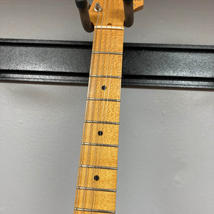 Close-up of a wooden neck with metal frets and dot inlays, hanging on a wall-mounted holder, featuring the iconic Fender 2006 Eric Johnson Stratocaster guitar's maple fingerboard.