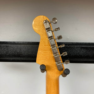 Close-up of the back of a 2006 Fender Eric Johnson Stratocaster headstock by Fender, featuring six metal tuning pegs and two padded hooks securing the maple fingerboard guitar against a wall.