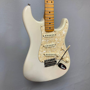 A 2006 Fender Eric Johnson Stratocaster by Fender, featuring a white finish, maple fingerboard, three single-coil pickups, white pearloid pickguard, and tremolo arm hangs on a gray wall.