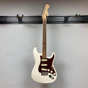 A Fender Limited Edition Ash American Professional Stratocaster in White Blonde with a dark red pickguard, three single-coil pickups, and a channel-bound neck hangs on a wall-mounted rack.