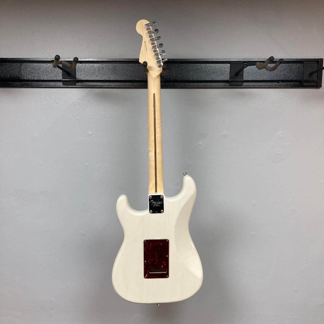 A Fender Limited Edition Ash American Professional Stratocaster White Blonde w/Case Consign is displayed from the back, hanging on a black metal wall rack against a plain light gray wall.