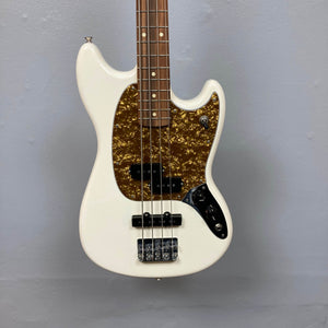 The Fender Mustang Player Bass PJ White Used by Fender features a short scale, PJ pickups, four strings, chrome hardware, and a brown-gold tortoiseshell pickguard, shown against a plain light gray wall.