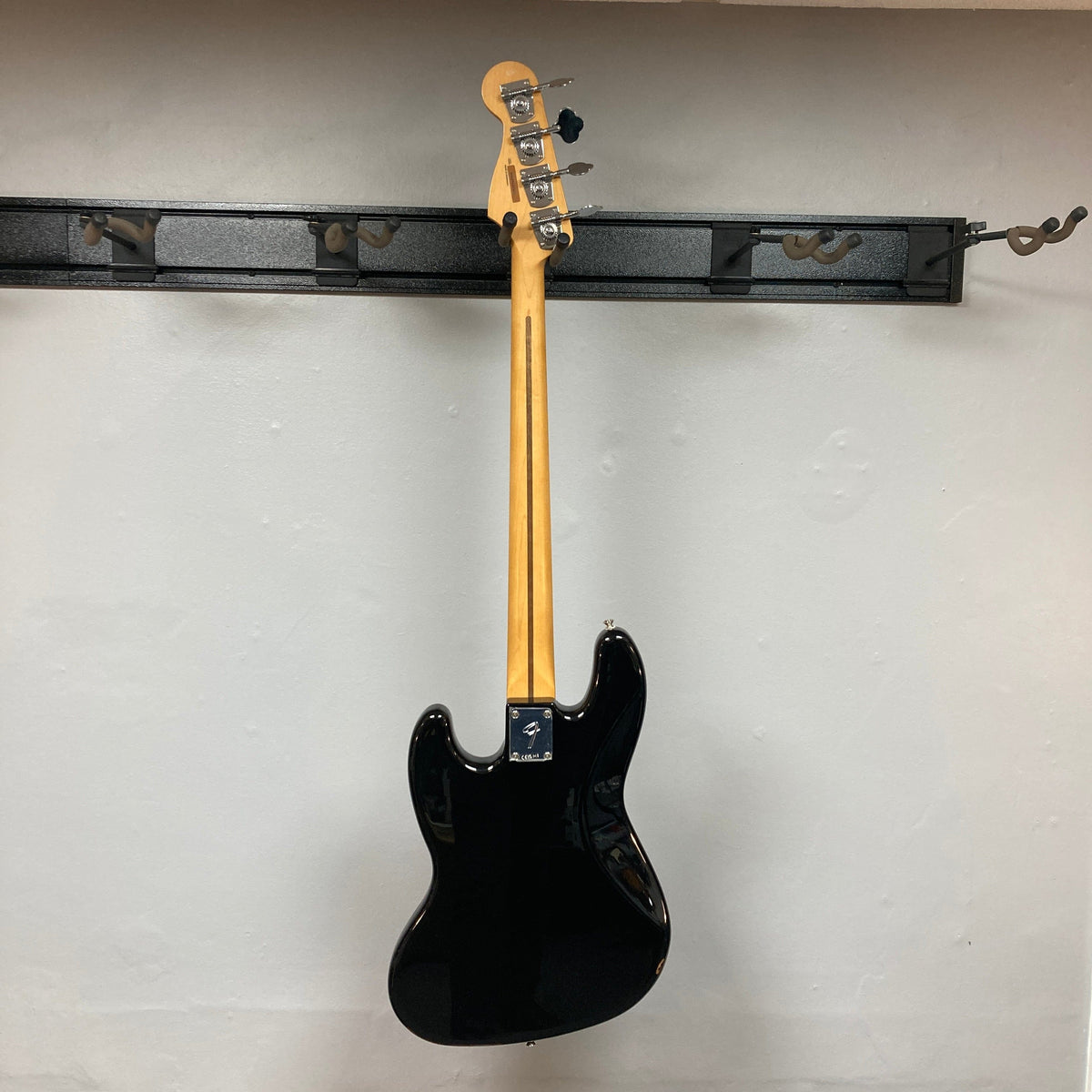 Fender Player II Jazz Bass Black Refurb displayed on a wall, showcasing its modern design and features like a contoured body and open-gear tuning machines.