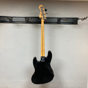 Fender Player II Jazz Bass Black Refurb displayed on a wall, showcasing its modern design and features like a contoured body and open-gear tuning machines.