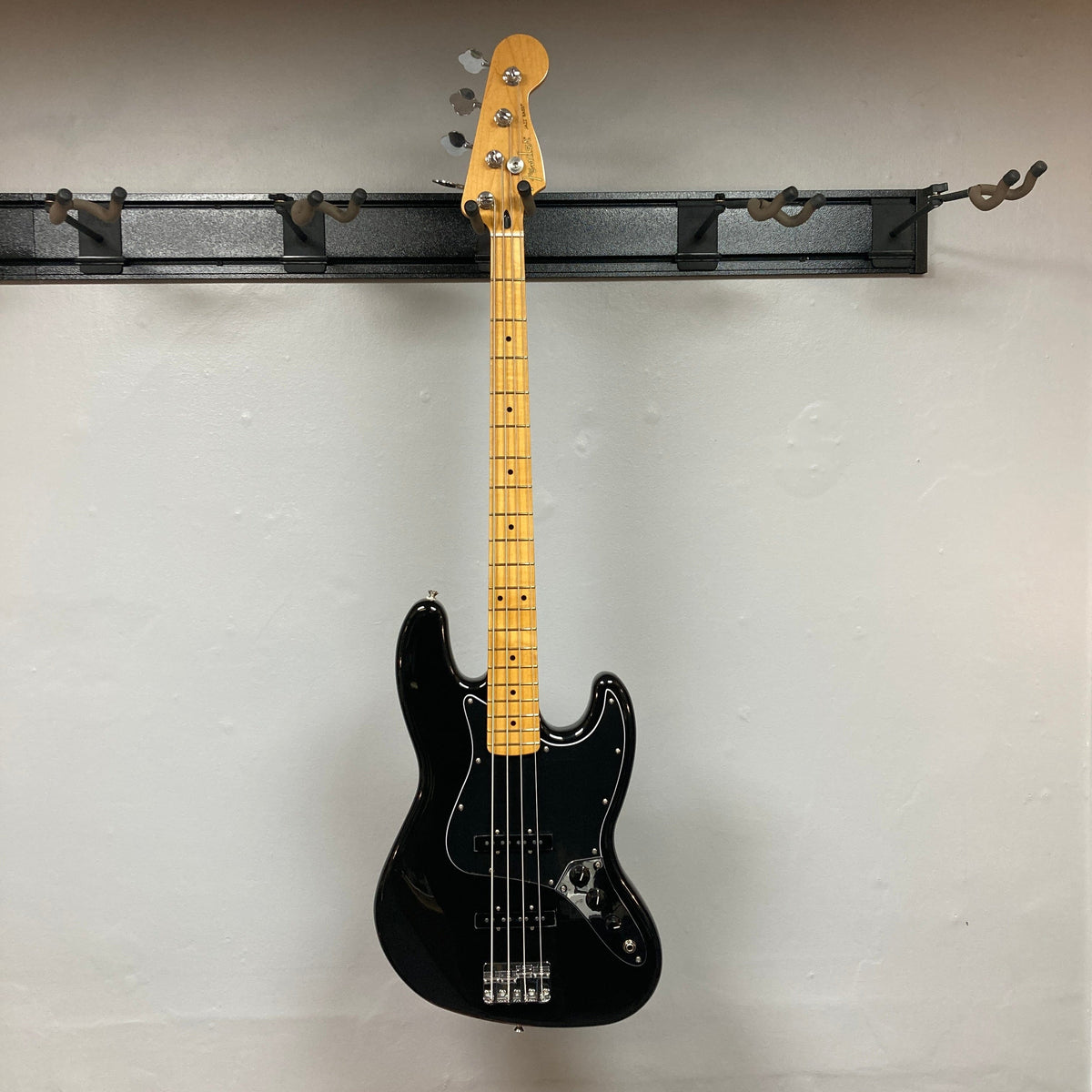Fender Player II Jazz Bass Black Refurb hanging on a wall, showcasing its contoured alder body and modern C neck profile with satin finish.