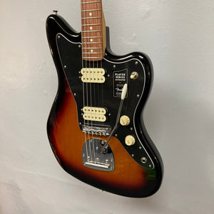 Fender Player Jazzmaster guitar, 3-tone sunburst, shown hanging on a wall, highlighting its body shape, strings, and white volume knob.