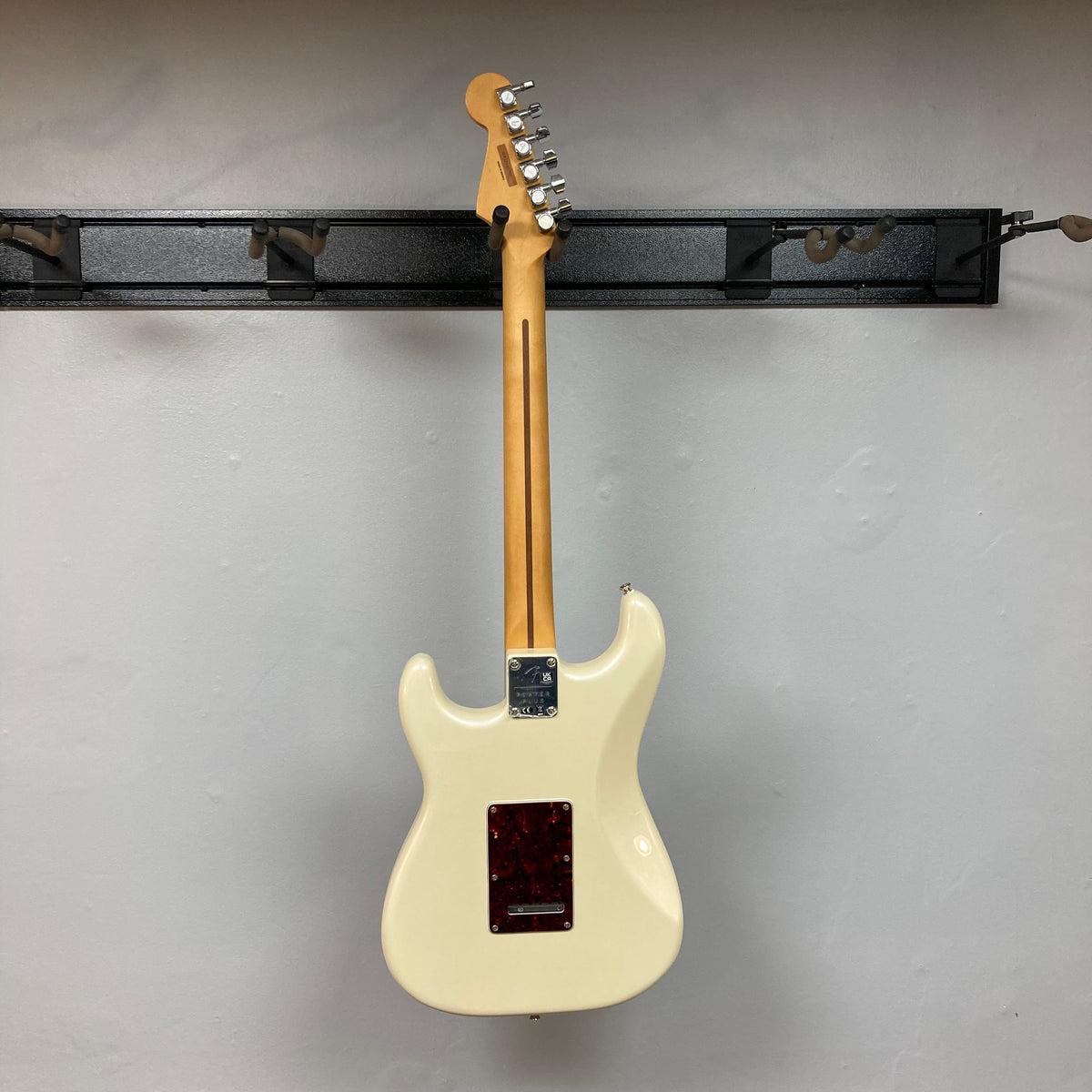 Fender Player Plus Stratocaster Olympic Pearl on black shelf, showcasing its sleek design and expert craftsmanship, includes gig bag.