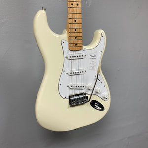 A Fender Standard Stratocaster Olympic White Refurb guitar by Fender, featuring a white finish and maple neck, is mounted against a gray wall.