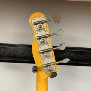 Close-up of the tuning pegs and headstock of the Fender Sting P Bass Sunburst by Fender, with its neck resting on a black guitar stand against a white wall.