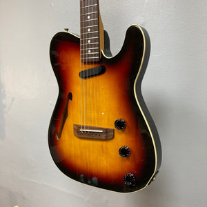 Fender Telecaster TLAC MIJ Acoustic/Electric Hybrid 1993-1997 3 Color Sunburst, hanging on a wall, showcasing its strings and black dials with white numbers.