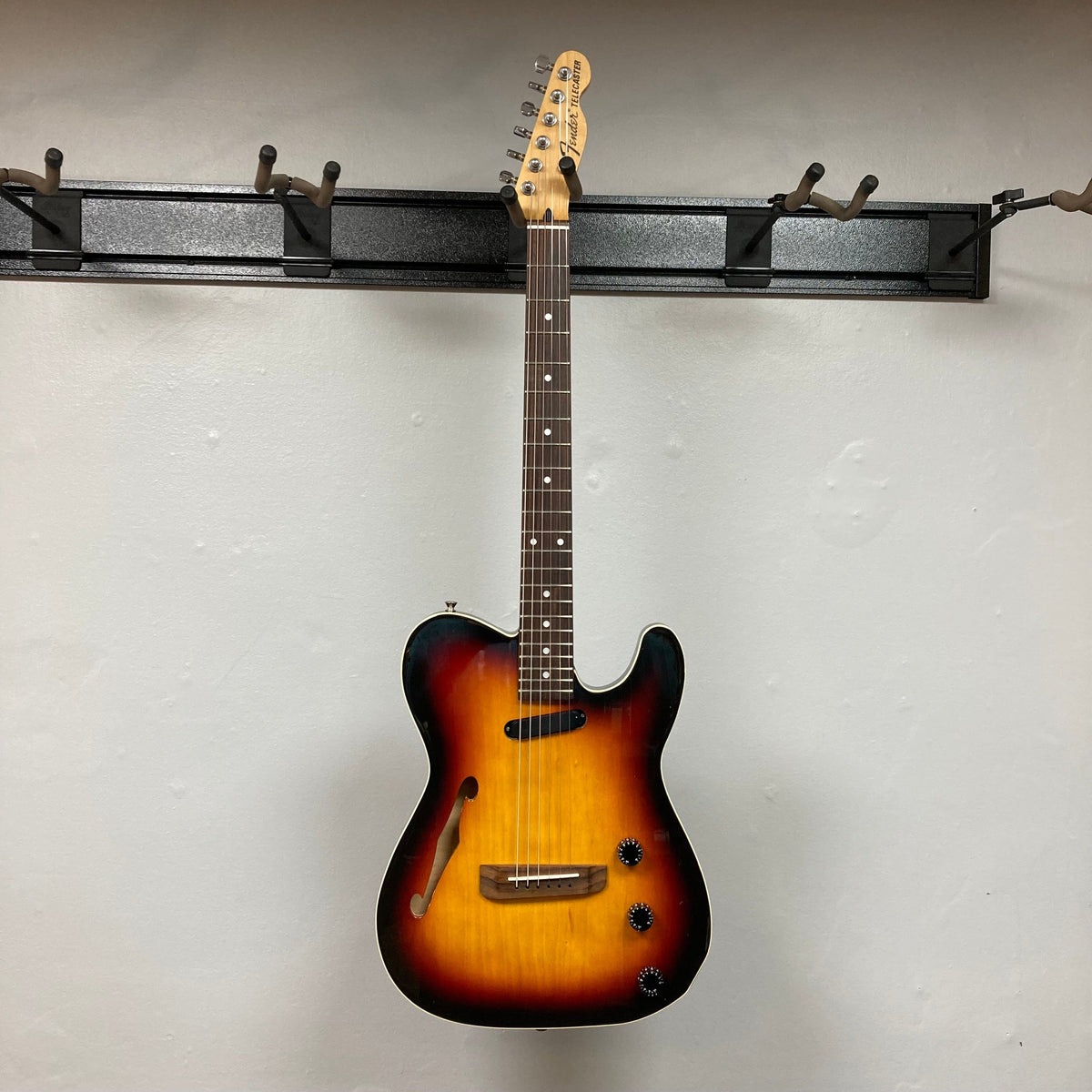 Fender Telecaster TLAC MIJ Acoustic/Electric Hybrid 1993-1997 on a hook, showcasing its solid body and detailed craftsmanship.