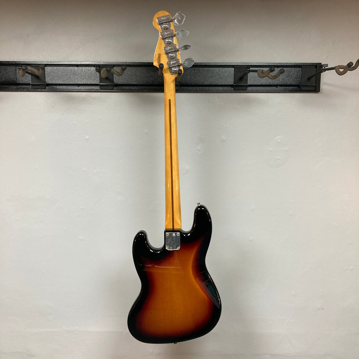 Fender Vintera '70s Jazz Bass on wall hook, showcasing its vintage-style neck and pickups, includes gig bag for protection.