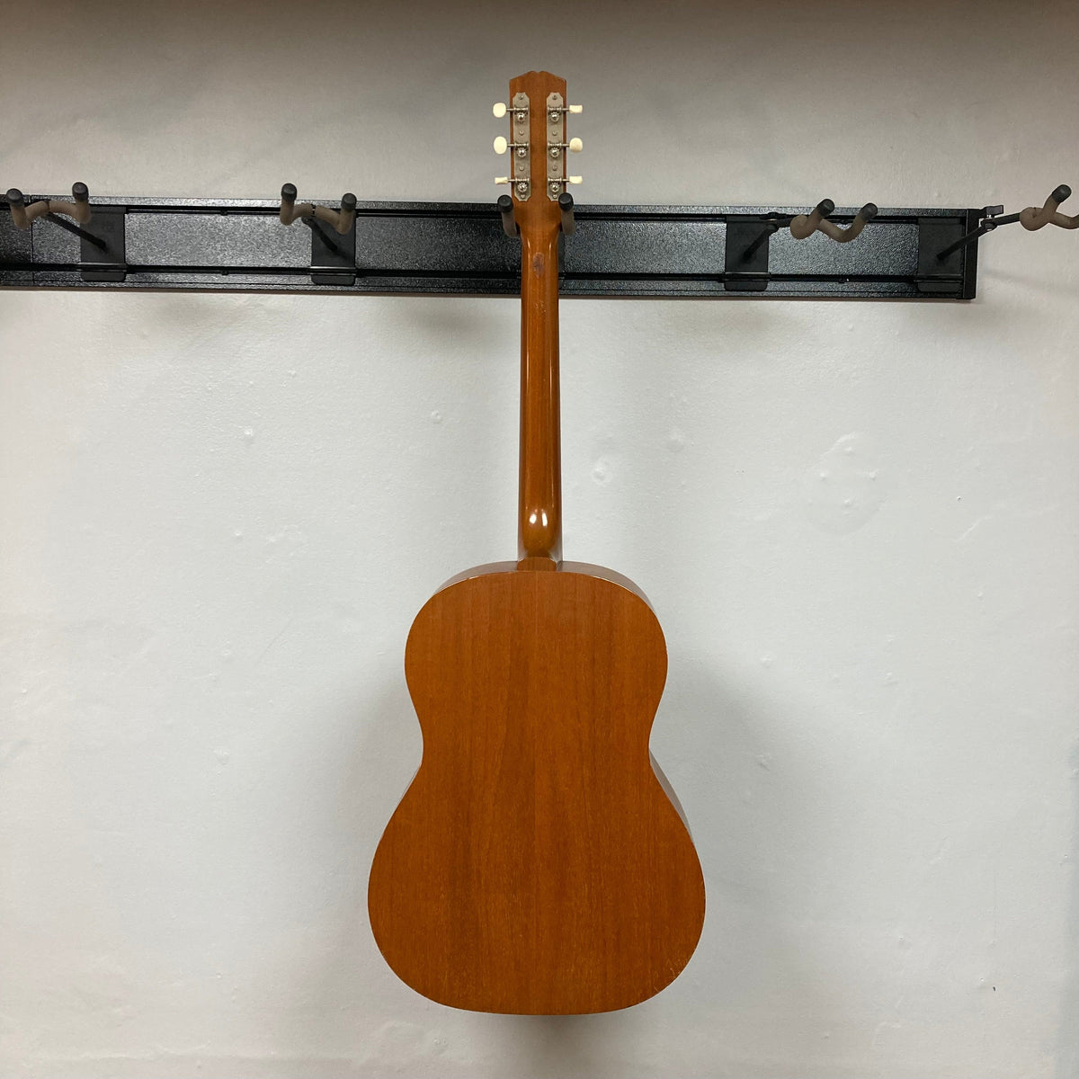 Gibson B-15 1967 - 1969 Natural w/Case, solid mahogany acoustic guitar on a hook, highlighting its vintage design and close-up detailing of wear.