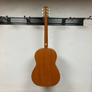 Gibson B-15 1967 - 1969 Natural w/Case, solid mahogany acoustic guitar on a hook, highlighting its vintage design and close-up detailing of wear.