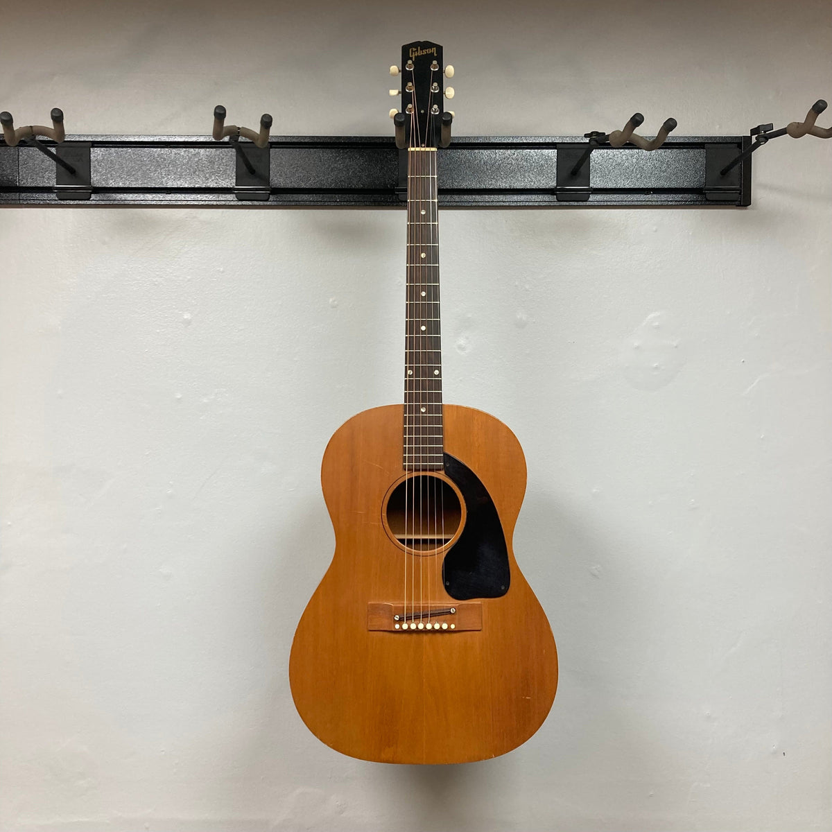 Gibson B-15 1967 - 1969 Natural w/Case, vintage acoustic guitar hanging on a wall, showing signs of wear and use.