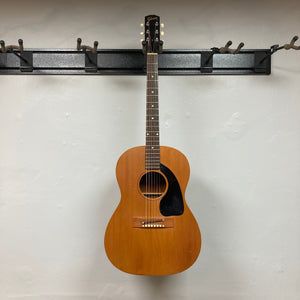 Gibson B-15 1967 - 1969 Natural w/Case, vintage acoustic guitar hanging on a wall, showing signs of wear and use.