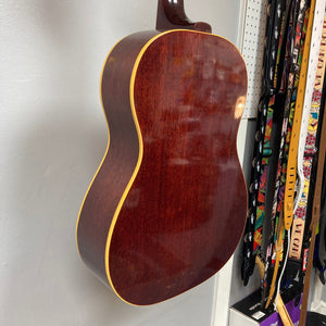 Gibson B-25 Acoustic Guitar Natural 1968 hanging on a wall, showcasing its vintage checking and craftsmanship.
